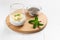 Chia pudding with banana in a glass cup with a sprig of mint and grains in a bowl on a wooden cutting board on a white background.