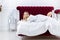 Chic blonde woman in luxury white with red bedroom. Rich expensive interior