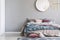 Chick round mirror on grey empty copy space wall in elegant bedroom interior with warm bed with blue, pastel pink and beige