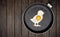 Chick-shaped fried egg in a pan on wooden background