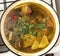 Chicken broth with pieces of meat on bone and vegetables in cooking pot, top view