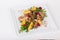 Chicken duck salad with arugula, raspberries, potatoes, sunflower seeds on a square white plate background