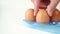 Chicken eggs in a blue plastic egg container, hand takes one brown egg