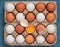 Chicken eggs in the carton box. Chicken egg is half broken among other eggs, eggshell and chicken feather near. Top view