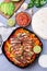 Chicken Fajitas with bell pepper and onion in a pan, served with salsa Asada, sour cream, avocado and tortillas, vertical, top