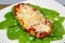 Chicken Parmesan on a bed of spinach with a sprinkle of fresh parmesan cheese on top on a white plate