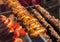 Chicken pieces being cooked for a barbecue. In the background other meats: Sausage, chicken heart