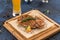 Chicken schnitzel grilled on wooden board with glass of beer on blue background