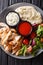 Chicken shawarma with hummus, vegetables and sauce serving on a plate close-up. Vertical top view