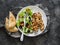 Chicken souvlaki kebabs, sun dried olives, tomatoes, cucumbers green salad and focaccia tortilla on dark background, top view