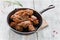 Chicken wings in cast-iron pan on wooden table. Marinated in tomato and honey sauce. Baked with sesame seeds