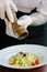 Chief hands dressing italian fettuccine pasta with pepper mill.