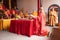 The chief monks bowing in front of the red table while holding a red paper for praying