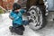 Child 10 years old repairs a car. Boy screws a nut on car wheel, snowy winter day. Replacement wheels in the snow