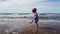 Child on ad the sea beach with rough sea have fun walking and jumping with a bandana and purple dress