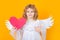 Child angel pointing on paper red heart, point gesture. Child angel. Portrait of cute kid with angel wings isolated on