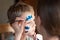 Child animator, artist`s hand draws face painting to little boy. Child with funny face painting. Painter makes blue batman mask o
