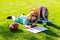 Child with artwork homework on playground. Clever school boy doing homework, writing on copy book in green grass of park