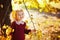A child in an autumn park flooded with the sun. A little blonde girl in a bard knitted sweater among yellow leaves