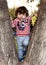 Child baby curly brunette in jeans and a T-shirt climbed a tree