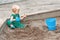 Child baby in sandbox playing with beach toys. Girl toddler watching exploring sand on hands. Kid have fun on playground. Summer