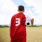 Child, back view and soccer player on field for training, workout and ready for practice on grass. Boy, athlete and ball