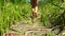 Child with bare feet walks along a wooden bridge on the river bank with reeds in summer.