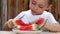 The child bites off a piece of watermelon. A piece of watermelon lies on a plate.