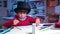 A child in a black top hat draws at a table
