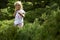 Child blond little girl picking fresh berries on blueberry field in forest.