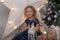 Child blonde in a blue dress with a flashlight near the Christmas tree in Christmas