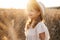 child blonde girl in straw hat and beige muslin dress in wheat field on sunset