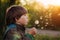 Child blowing on a dandelion. Kid with a flower at sunset in the summer. Autumn Glow Sunshine. Pollen allergy