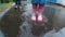 Child in boots walking and jumping in muddy puddle after rain.