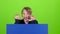 Child boy appeared from behind a blue poster grins curves of faces and hidden again. Green screen. Slow motion