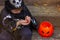 child boy in black halloween costume unwrapping candy sitting on steps near pumpkin bucket