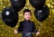 child boy holding black balloons on background with gold shiny sequins, paillettes.