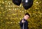 child boy holding black balloons on background with gold shiny sequins, paillettes.