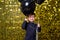 child boy holding black balloons on background with gold shiny sequins, paillettes.