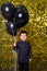 child boy holding black balloons on background with gold shiny sequins, paillettes.