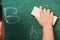 Child boy kindergarten in student uniform wiping clean or erase chalk on green school blackboard