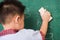 Child boy kindergarten in student uniform wiping clean or erase chalk on green school blackboard