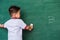 Child boy kindergarten in student uniform wiping clean or erase chalk on green school blackboard