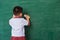 Child boy kindergarten in student uniform wiping clean or erase chalk on green school blackboard