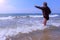 Child boy plays and jumps through waves at sea sandy beach in windy spring day.