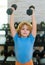 Child boy pumping up biceps muscles with dumbbell. Fitness kids with dumbbells.