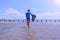 Child boy on sea vacation walks at sea water in wet t-shirt on sandy beach.