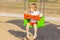 Child boy sits on a bright swing on the playground on the beach. concept of childhood, summer vacation and activities