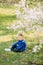 Child boy sits on sunlit glade in blooming garden