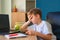 Child boy sitting at wooden table, tired from doing homework at home